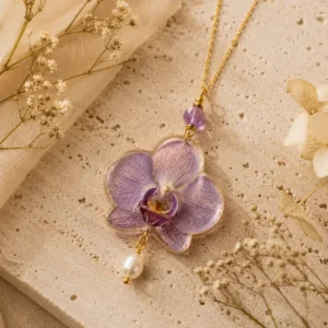 Collar artesanal con orquídea natural preservada en tonos violetas sobre piedra travertino y detalles dorados