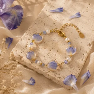 Pulsera artesanal inspirada en flores de iris azules preservadas con detalles dorados, perlas y cristales sobre travertino beige