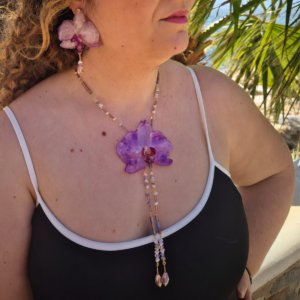 Modelo luciendo el conjunto Vaiana compuesto por un collar con orquídea natural fucsia y flecos de cuentas de cristal junto a unos pendientes colgantes de orquídea reales a juego.