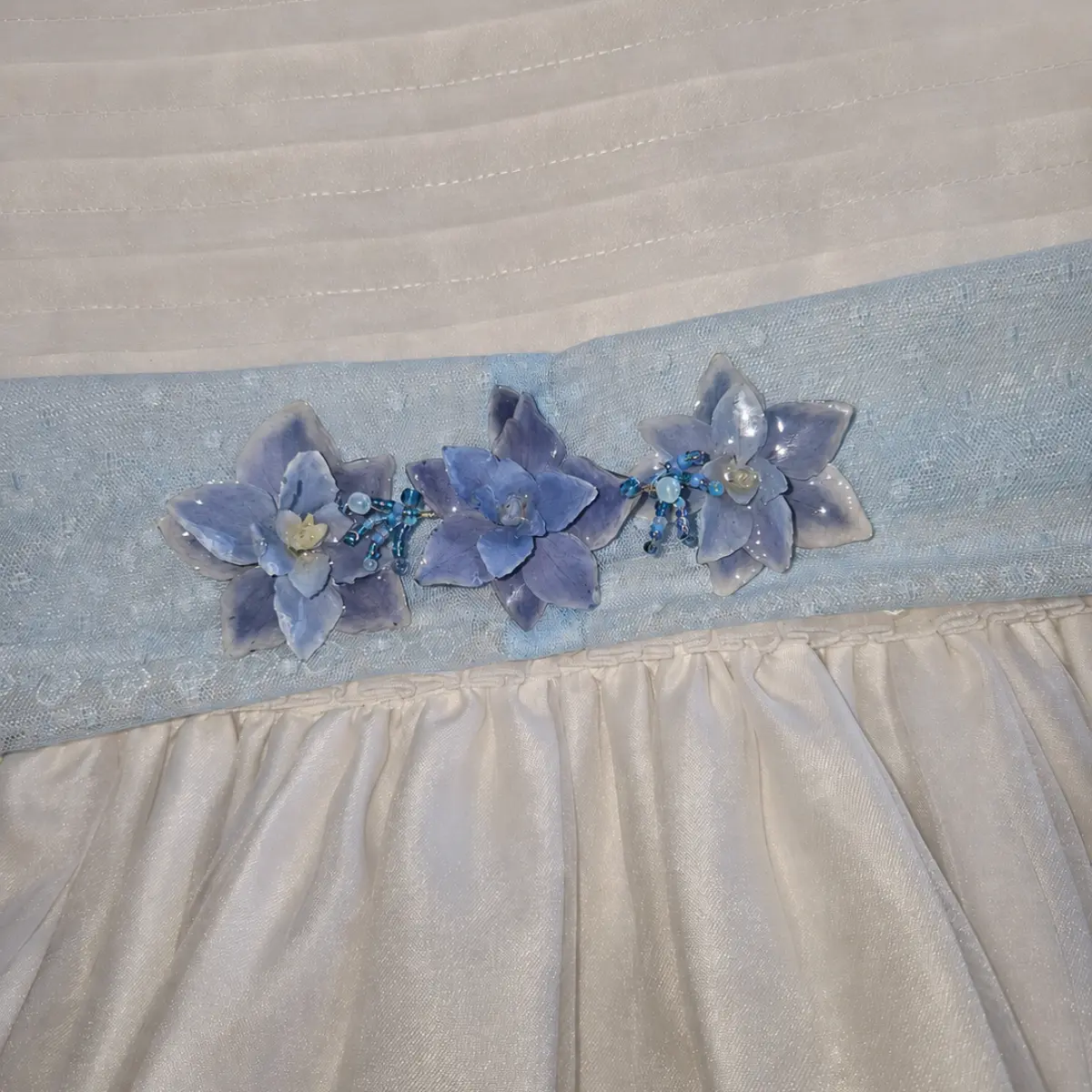 Detalle de las tres flores naturales encapsuladas en resina del cinturón de comunión azul cielo sobre el cuerpo del vestido.