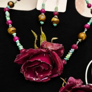 Conjunto de collar, pulsera y pendientes con rosas naturales rosas encapsuladas en resina transparente sobre fondo blanco.